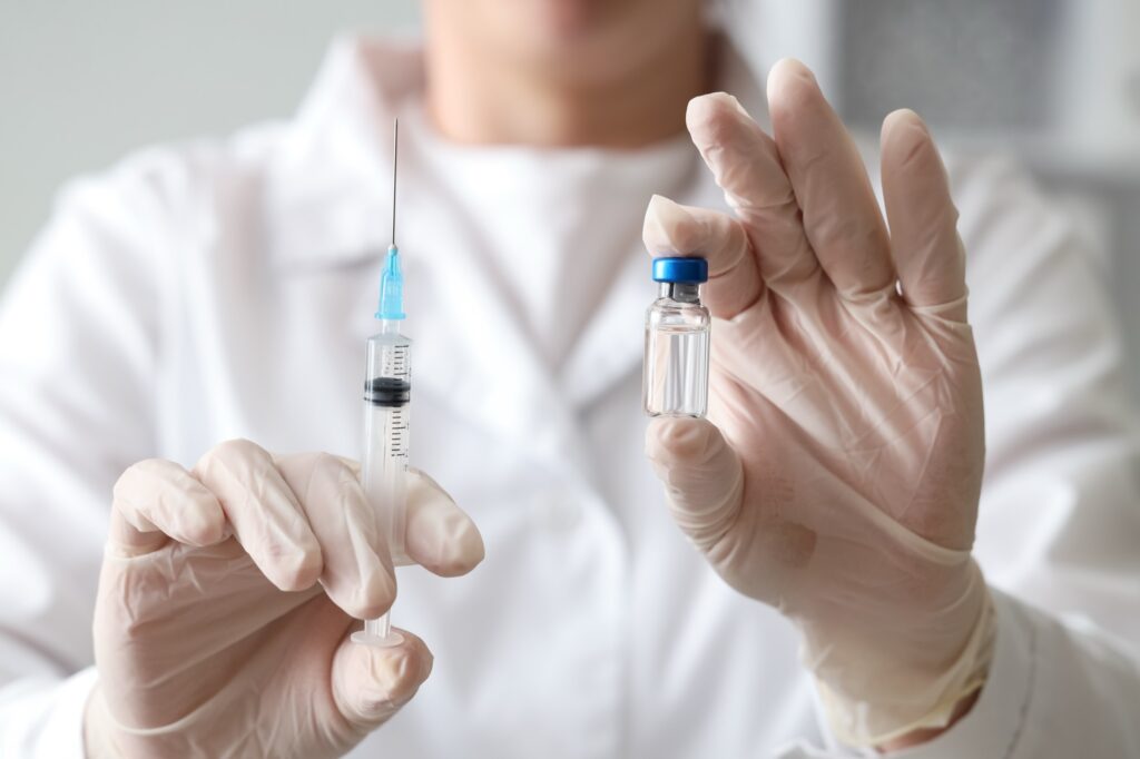 Pracownik medyczny w białym fartuchu laboratoryjnym i rękawiczkach, trzymający strzykawkę i przezroczystą fiolkę ze szczepionką, służbę zdrowia i immunizację