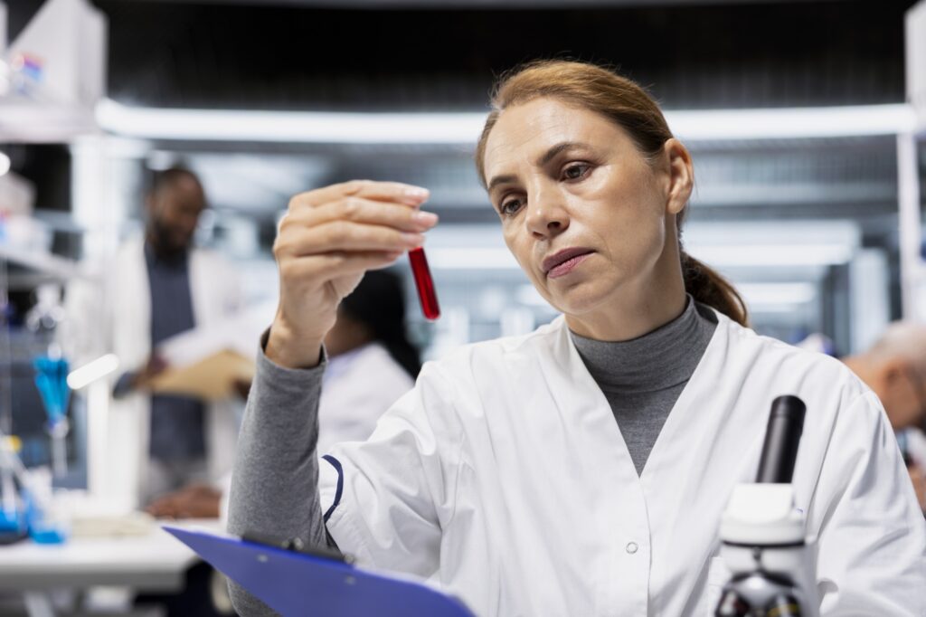 Farmaceuta testuje próbki krwi pod kątem niepożądanych reakcji na lek w ramach próby klinicznej, podczas gdy kierownik laboratorium w średnim wieku ocenia fiolki z płynem w celu weryfikacji standardów bezpieczeństwa leków