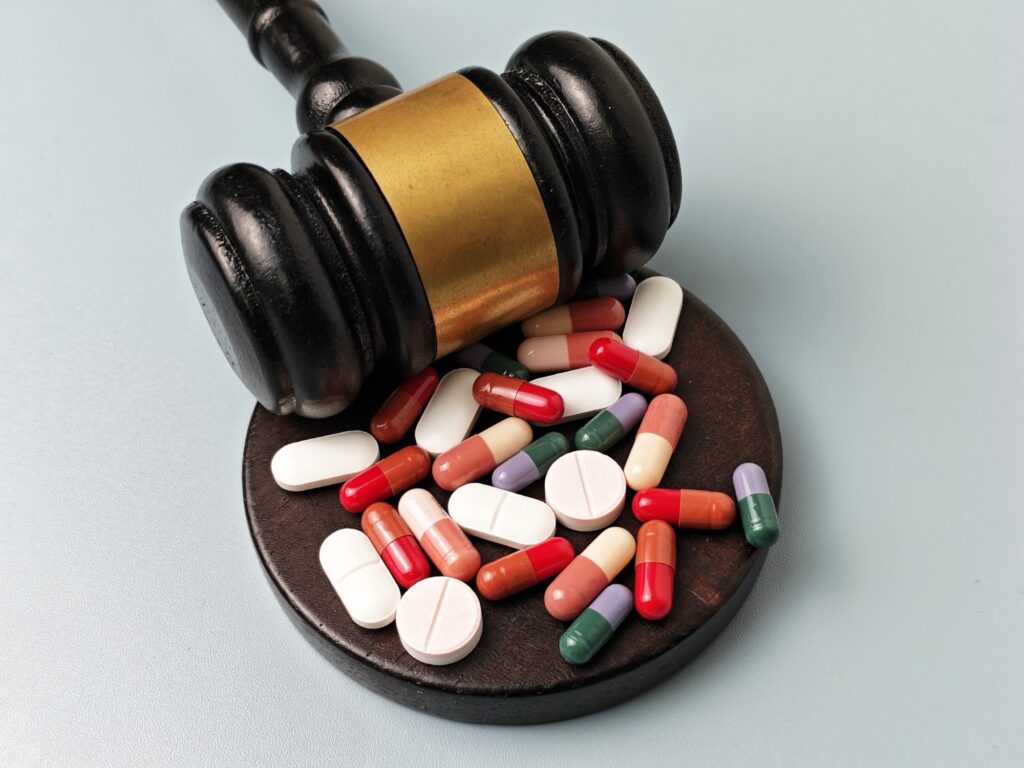 Sędzia gavel z pigułkami i kapsułkami na czystym białym tle reprezentujący prawo farmaceutyczne, regulację leków, opiekę zdrowotną i zgodność z prawem