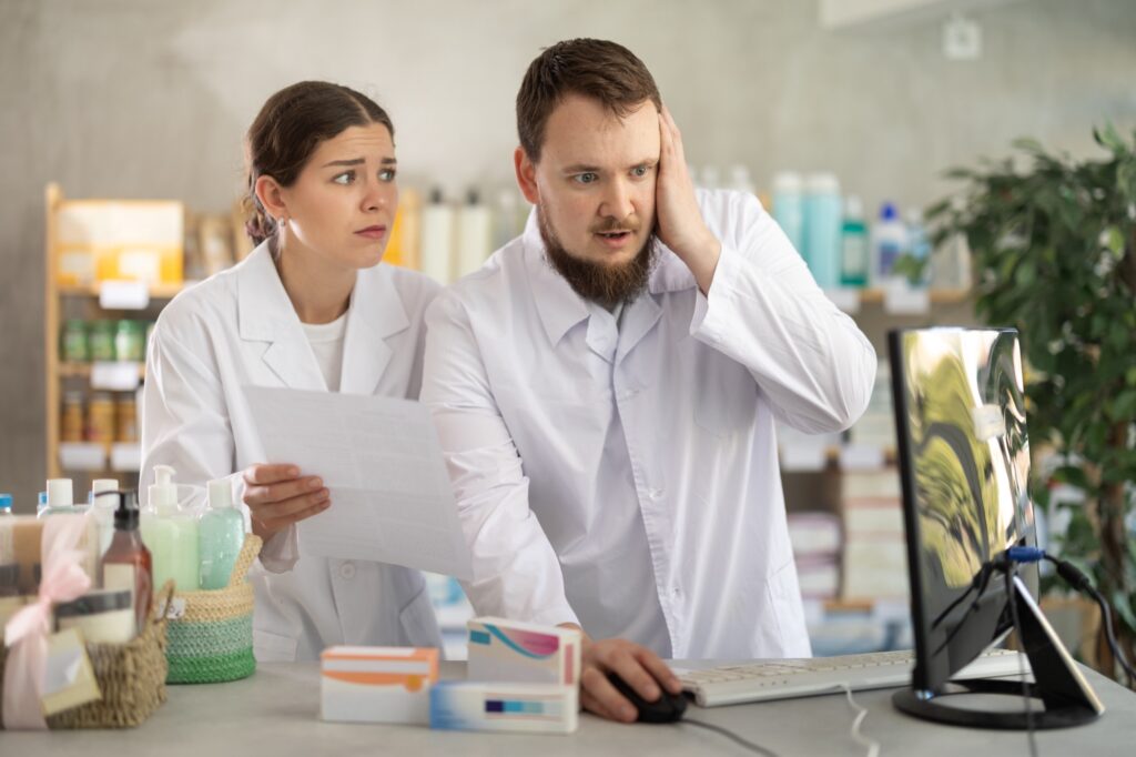 Dwóch farmaceutów pracuje w aptece i próbuje rozwiązać błędy w systemie komputerowym i zaktualizować go. mężczyzna i kobieta farmaceuta są zdenerwowani niewłaściwą ilością towarów w magazynie